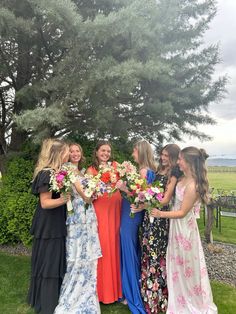 a group of women standing next to each other holding bouquets in front of a tree