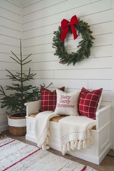 a white bench with christmas pillows and a wreath on the wall next to it,