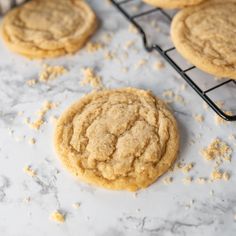 three cookies cooling on a rack with some oatmeal scattered around them and one cookie in the foreground