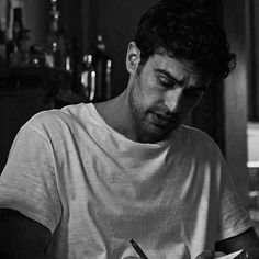 a man sitting at a table with a pen in his hand and writing on paper