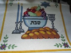 a cross - stitch table cloth with an image of bread and fruit in a bowl