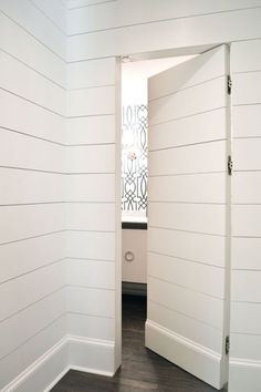 an open door leading into a white room with wood flooring and shiping on the walls