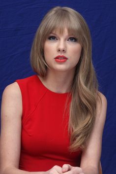 a woman in a red dress sitting down with her hands on her lap and looking off to the side