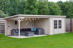 an outdoor living area with couches and tables in the grass next to a wooden fence