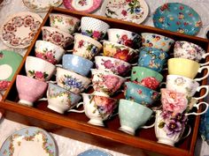 a wooden box filled with lots of colorful cups and saucers on top of a table