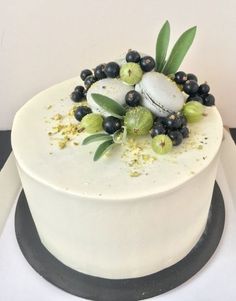 there is a white cake with black berries and green olives on the top layer