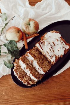 slices of carrot cake with frosting on a black plate next to apples and leaves