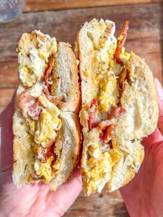 two halves of a toasted sandwich with eggs and bacon on it, held in someone's hand