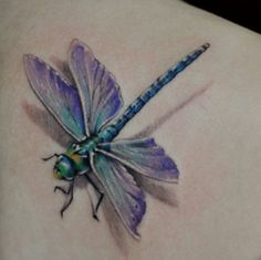 a blue and green dragonfly tattoo on the back of a woman's shoulder