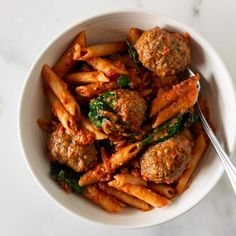 pasta with meatballs and spinach in a white bowl on a marble countertop