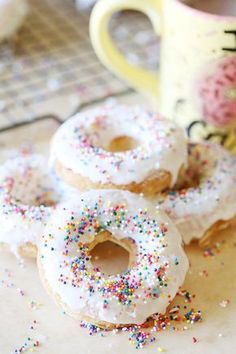 three donuts with white frosting and sprinkles next to a coffee cup