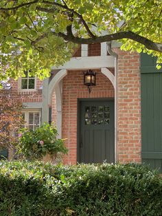 a brick house with green shutters and a light fixture on the front door is surrounded by greenery