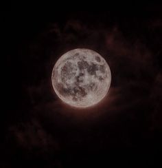 the full moon is seen through clouds in this dark night time photo, with only one light visible