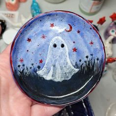 a hand holding a small glass plate with a ghost painted on it's side