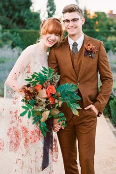 a man and woman standing next to each other in front of some bushes with flowers