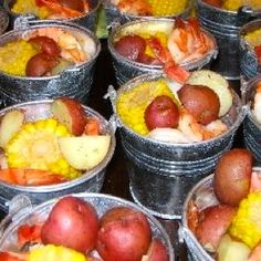 several buckets filled with different types of food on top of a wooden table next to corn and potatoes