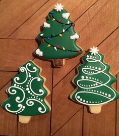 three decorated cookies sitting on top of a wooden table next to each other with christmas trees painted on them