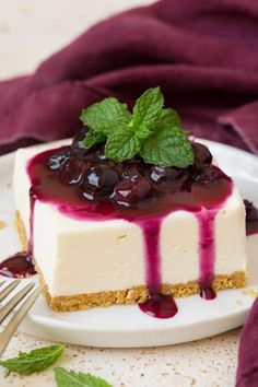 a white plate topped with a cheesecake covered in blueberry sauce and fresh mint