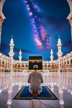 a man sitting on top of a rug in front of a building with a sky filled with stars