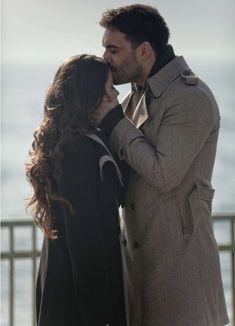 a man and woman kissing each other with the ocean in the back ground behind them