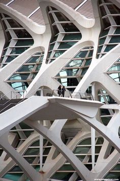 two people are standing on a bridge in front of a large building with many windows