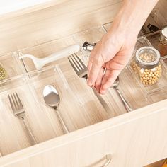 a person reaching for food in a drawer with utensils and spoons on it