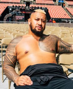 a man with tattoos sitting on a chair in front of an empty bleachers