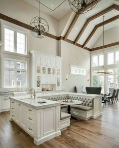 a large open kitchen with white cabinets and wood flooring, along with two chandeliers hanging from the ceiling