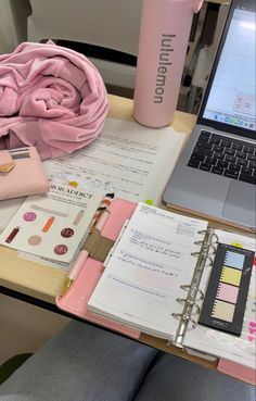 a laptop computer sitting on top of a desk next to a pink towel and notebook