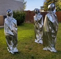 two silver statues covered in plastic standing on grass