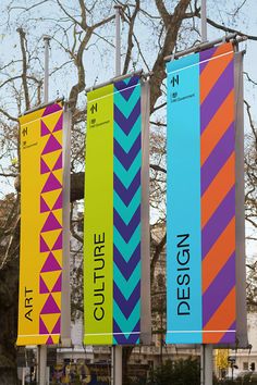 three colorful banners are hanging on poles in front of a tree with no leaves or branches