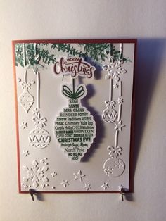 a christmas card with an ornament hanging from the side on a white wall