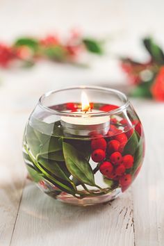 a glass bowl filled with water and red berries on top of a white wooden table