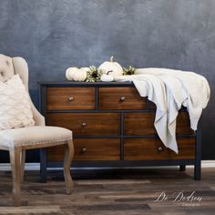 a chair sitting next to a dresser with a blanket on it and pumpkins in the background