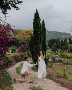 a man kneeling down next to a woman in a white dress on a dirt road