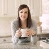 a woman sitting at a kitchen counter drinking from a cup and saucer with her hands in the air