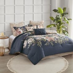 a bed with blue comforter and pillows in a room next to a plant on the floor