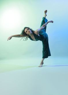 a woman in a green dress is doing a handstand on one leg with her arms outstretched