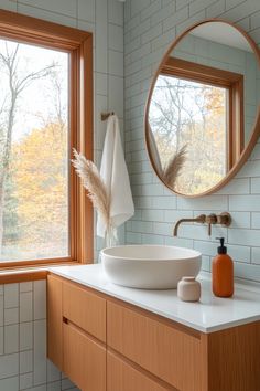 a white sink sitting under a round mirror next to a wooden cabinet and counter top