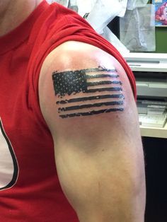 a man wearing a red shirt with an american flag tattoo on his arm