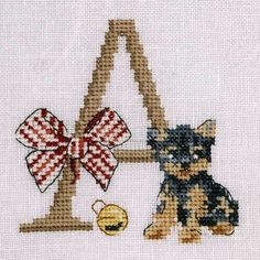 a cross stitched picture of a dog with a bow sitting next to a letter