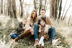 a family sitting in the woods with their two children and one dog, all looking at the camera