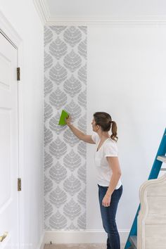 a woman is painting a wall with white and gray stencils on the walls