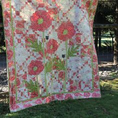 a red and white quilt with flowers on it hanging from a clothes line in the grass