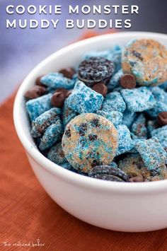 a white bowl filled with blue and brown muddy buddies next to an orange napkin on top of a table