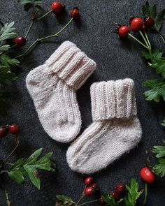 two white knitted baby mittens laying on top of holly leaves and red berries