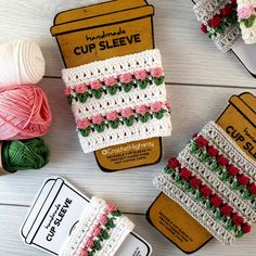 crocheted cup sleeves with pink roses and green leaves on them next to yarn