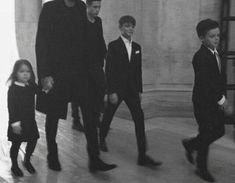 a black and white photo of three young boys in suits walking down the street with their parents