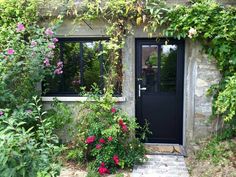 a black door surrounded by flowers and greenery in front of a stone building with windows