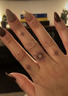 a woman's hand with two small stars on it and a sun tattoo on the middle finger